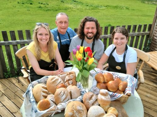 Group smiling at camera in black aprons with bread products on the table